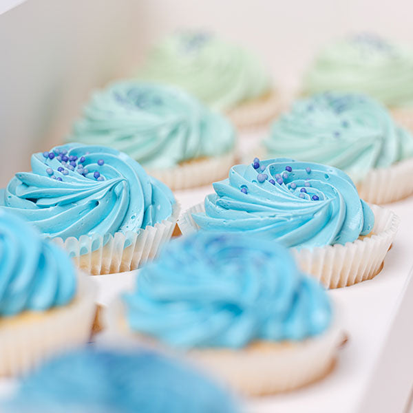 Cupcakes topped with varying shades of ombre Blue colours, topped with blue edible sprinkles. 